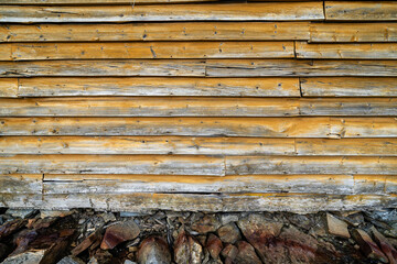 Facade of an old wooden building of Scandinavian type with yellow wooden boards, where there is a stone wall at the bottom