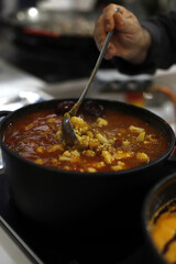 cazuela de garbanzos y arroz con verduras en fogón de restaurante removiéndolo el chef con un cucharon