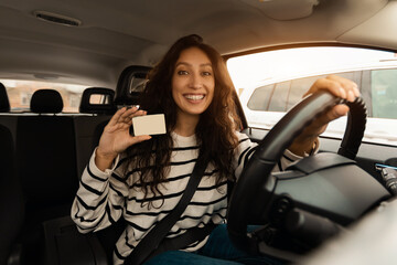 Smiling female driving new car showing driver license