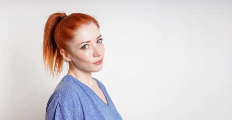young woman with red hair tied in ponytail tilts her head smiling - obrazy, fototapety, plakaty