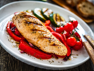 Grilled chicken breast with pepper, zucchini and cherry tomatoes on wooden table
