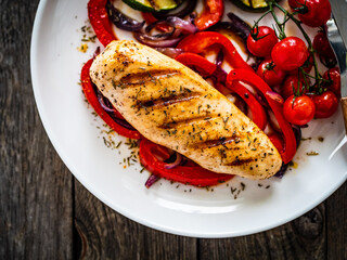 Grilled chicken breast with pepper, zucchini and cherry tomatoes on wooden table
