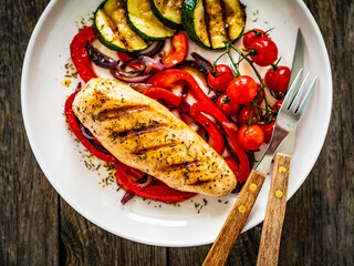 Grilled chicken breast with pepper, zucchini and cherry tomatoes on wooden table
