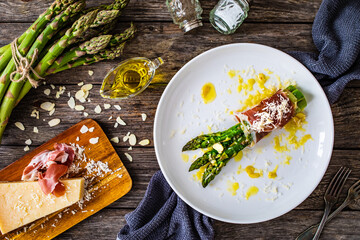 Cooked green asparagus, prosciutto di Parma and parmesan on wooden table
