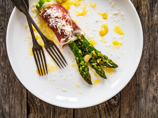 Cooked green asparagus, prosciutto di Parma and parmesan on wooden table
