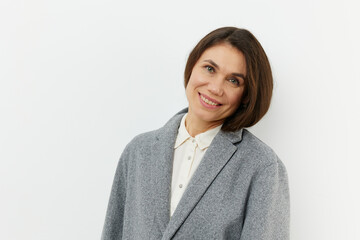 portrait of a cute, happy, pleasant woman smiling happily at the camera while standing in a gray coat on a pale background with an empty space for an advertising mockup