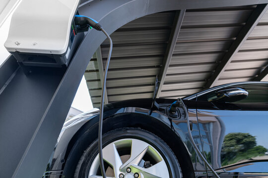 Electric car is charged from a charging station at carport that takes energy from solar panels. Close up