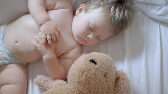 cute little boy sleeps sweetly in crib sees colorful dream Sleeping baby happy and carefree in bed hugging teddy bear toy. Mother cover with blanket child. Happiness sleep, children without coughing.