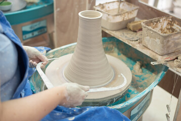 Master works on potter's wheel, doing blank. Hands of person sculpt vase from white clay. Workshop for manufacturing potter's products. Concept of creative, skill and handmade.