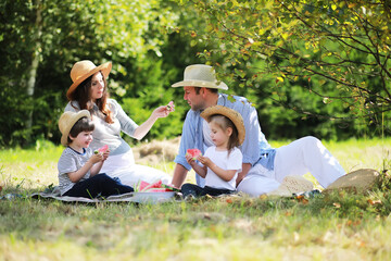 Happy family with children having picnic in park, parents with kids sitting on garden grass and eating watermelon outdoors