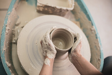 Master works on potter's wheel, doing bowl. Hands of person sculpt pot from white clay. Workshop for manufacturing potter's products. Top view. Concept of creative, skill and handmade.