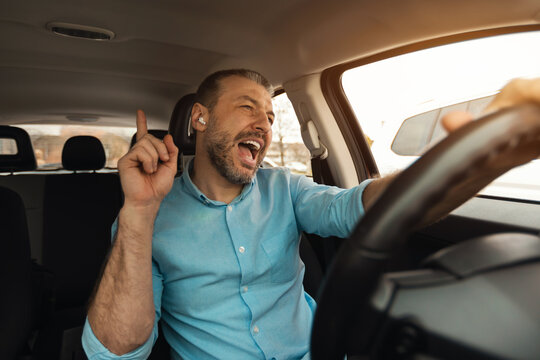 Happy man in earphones enjoying music driving luxury car