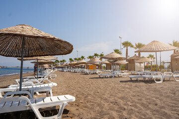 View of touristic beach with sun beds and wicker umbrellas on the sand and blue sky. Copy space. The concept of a sea beach holiday. Wallpaper.