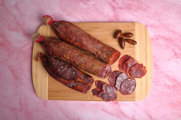 Iberian chorizo, Iberian salami and Iberian tenderloin on cutting board and pink marble table.