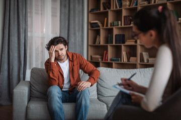 Young european female psychologist consults unhappy caucasian man in modern clinic interior