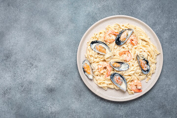 Fettuccine pasta in a creamy sauce with seafood in a plate on a gray concrete background. Pasta with shrimps and mussels. Top view, flat lay.