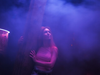 A woman stands embracing a tree trunk in a night theatrical mystical haze.