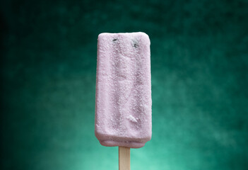 hand holding a sweet potato flavor popsicle with tapioca on a gradient green background