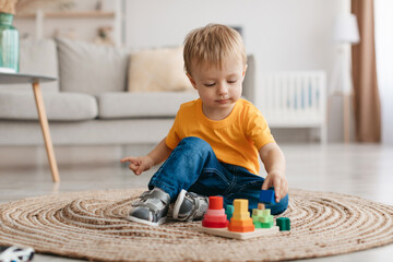 Early development concept. Little toddler boy playing with educational wooden toy at home, sitting...