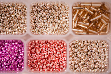 Small tiny colorful glass beads in plastic box container close up top view. Background and texture.