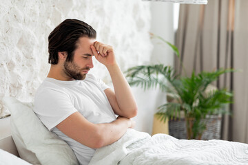 Thoughtful millennial guy staying in bed at home