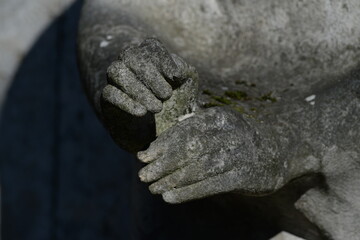 Partial view of an old, weathered sandstone sculpture. Hands in front of a dark background. 