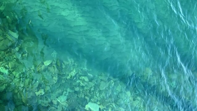 Stones under water. Seabed top view. Ocean on a sunny day in summer. Water surface. Wind waves. Nature without people. Vacation on the beach. Clear water. The bottom is visible.