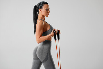 Athletic girl working out with resistance band on gray background. Fitness woman exercises with...