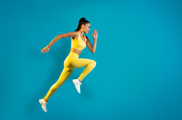 Fototapeta na wymiar Sportswoman Jumping In Mid Air Exercising Over Blue Background