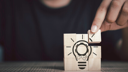 Innovative technology. Inspiration, brainstorming creative ideas for new innovations concept. Hand hold gear in light bulb icon on  wood cube with black background. Copy space...