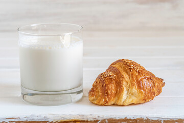 Sweet croissant and glass of milk on white wooden background.