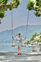 young woman in a dress sits on a swing near the lake