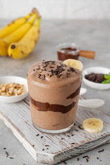 Vegan banana chocolate ice cream with chocolate glaze and sprinkles in a glass on a gray concrete...