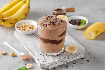 Vegan banana chocolate ice cream with chocolate glaze and sprinkles in a glass on a gray concrete background. Healthy food. Copy space.