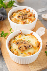 Baked julienne with mushrooms and chicken in a creamy sauce with cheese on top on a gray concrete background. Selective focus. Copy space.