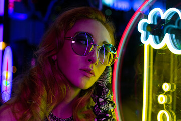 Long hair girl with sunglasses and leather jacket looking at neon lights
