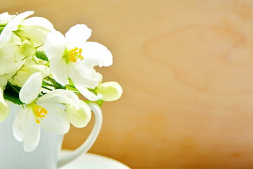 Macro of petals of apple blossoms stacked in white cup on wooden board blurry background with copy space