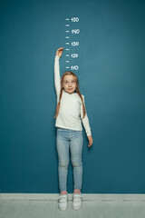 Child girl measuring the growth on the background of wall at home. Girl power concept.