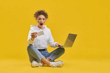 Surprised girl looking at credit card, while making online purchase inside. Front view of shocked...