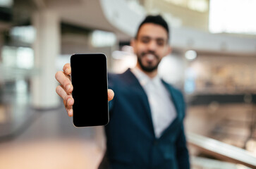 Happy confident millennial islamic businessman in suit with beard show phone with empty screen