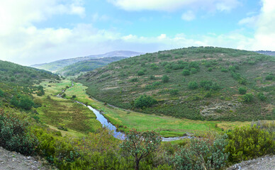 Panoramic of a river running through the meadow in a green valley with mountains in the background.
