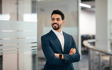 Cheerful confident handsome millennial muslim businessman with beard in suit with crossed arms