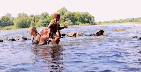 a mother with her children swims in the river and plays a selective trick on a summer day, a family...