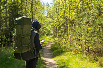 Tourist, traveler listens to music in headphones with a backpack on his back in the forest. And he holds the phone in his hands.