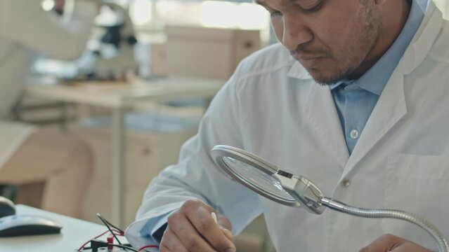Medium closeup with slowmo of Biracial male engineer cleaning inside printed circuit board with cotton swab while repairing it in laboratory