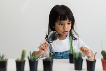 kid gently touch new stem of the cactus he grows with care, one hand holds magnifying glass.Nature...