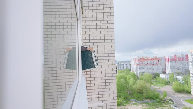 Installation of the air cooling system in the apartment, the man master takes the air conditioner out the window and fastens the ugo on the wall of the house at a high altitude. conditioning systems
