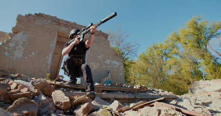 A Ukrainian soldier with a rifle pointed in front of him leaves the destroyed house and aims at the...