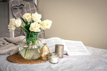 Home composition with a bouquet of tulips in a glass vase and candles.