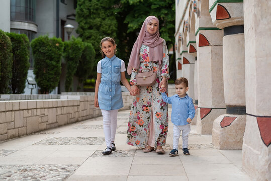 Happy Muslim Family Mom In Hijab Walking And Holding Hands With Two Children Outdoor.	